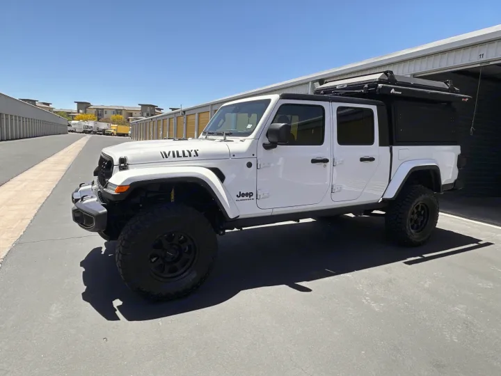 White Jeep Gladiator adventure RV rental with rooftop tent and camper setup, parked by storage units on a sunny day.. Jeep Gladiator Willys 2024