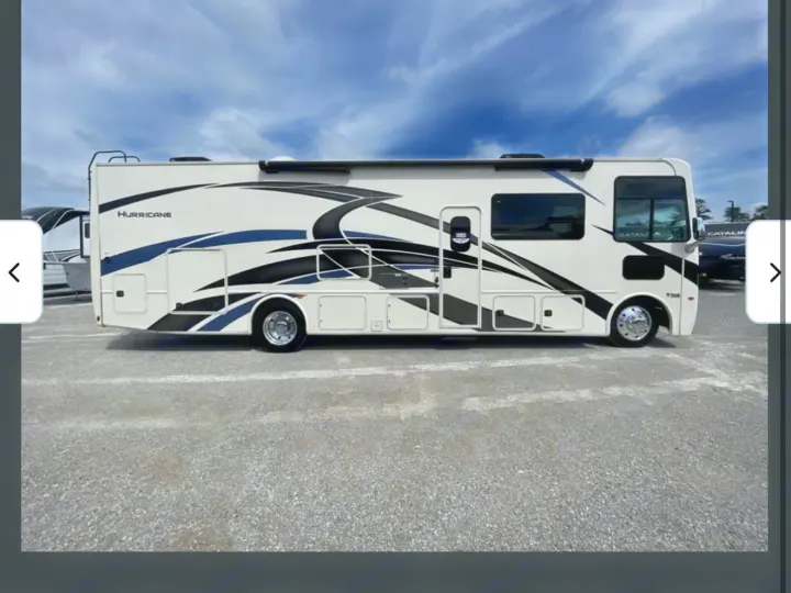White Hurricane RV rental, a sleek motorhome with blue and black graphics, parked on an asphalt lot. Perfect for your next trip.. Thor Hurricane 2022