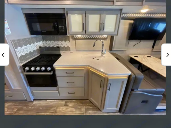Modern RV rental kitchen featuring a stove, microwave, sink, light countertops, and a cozy dining booth.. Thor Hurricane 2022
