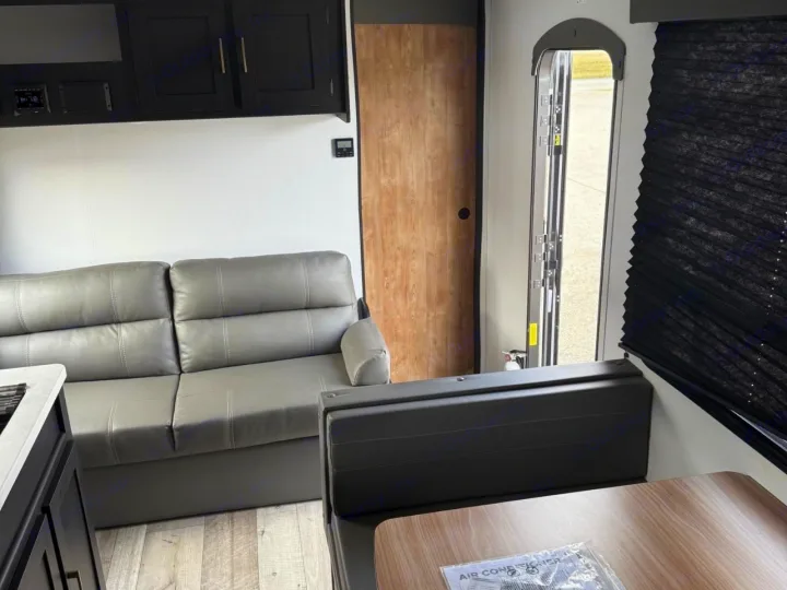 RV rental interior with a gray sofa, dinette, black cabinets, and an open exterior door. Features light wood accents and flooring.. Keystone RV Springdale 2022