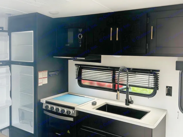Experience our modern RV rental kitchen. Sleek black cabinets, white counters, sink, stove, fridge, and microwave. Ready for your adventure!. Keystone RV Springdale 2022