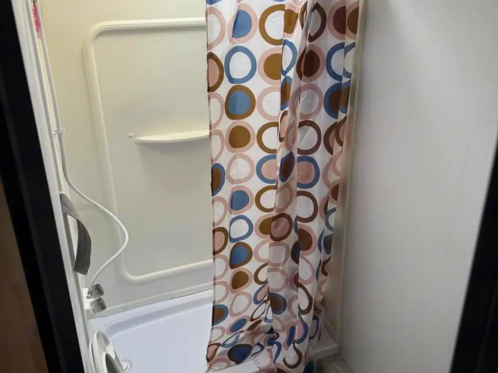 RV rental bathroom features a clean, compact shower stall with a circular-patterned curtain and handheld sprayer.. Keystone RV Springdale 2022