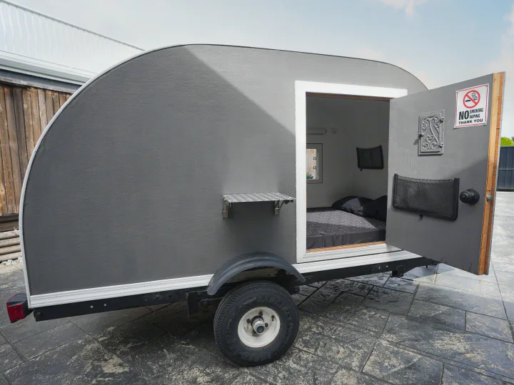 A gray teardrop rv rental with open door reveals a cozy bed. Features an exterior shelf & 'no smoking' sign on the door.. Micro-Lite Micro Camper 1987