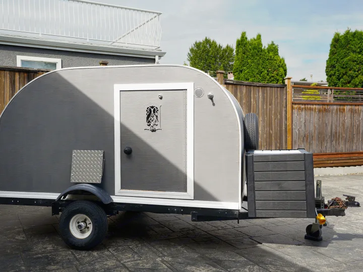 This grey teardrop trailer, featuring a side door and spare tire, is perfect for your next RV rental adventure.. Micro-Lite Micro Camper 1987