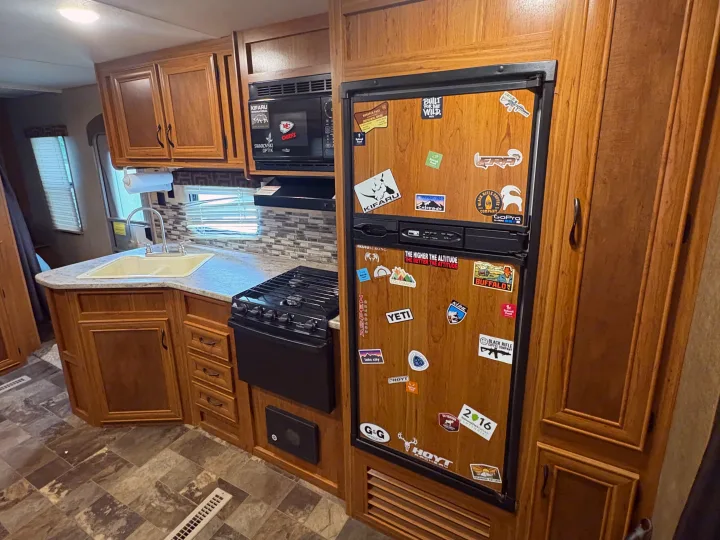 Cozy RV rental kitchen featuring wood cabinets, microwave, stove, and a sticker-covered fridge, ready for adventure.. Starcraft AR-One Maxx 2016