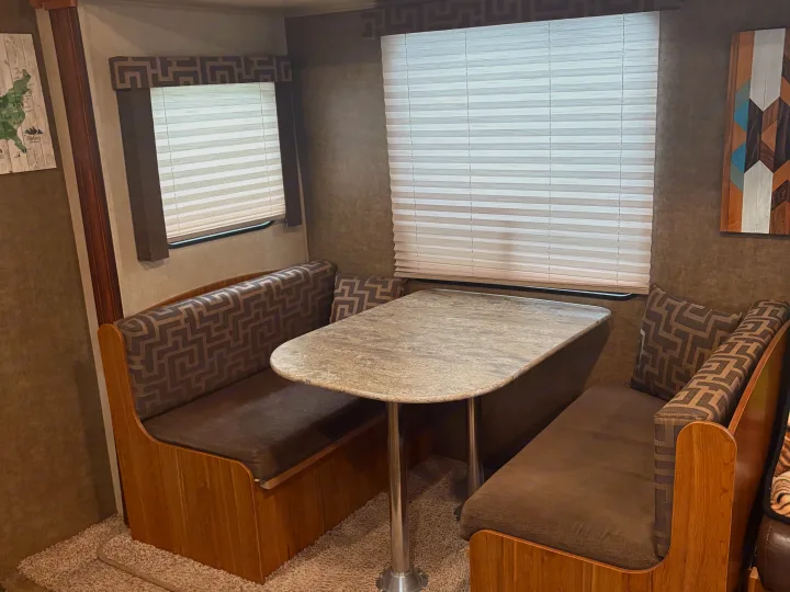 This RV rental dinette features wood-paneled bench seats with patterned cushions, a stone-look table, and white window blinds.. Starcraft AR-One Maxx 2016