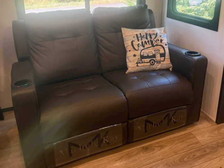 Plush brown leather two-seater recliner sofa with cup holders & a "Happy Camper" pillow in this cozy RV rental.. Forest River Sabre 2025