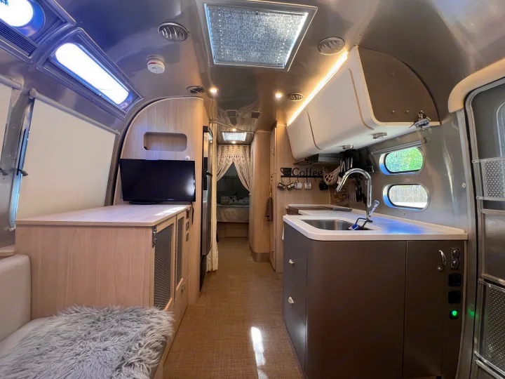 Spacious rv rental interior featuring a modern kitchen, living area with TV, and cozy bedroom at the end of the hall.. Airstream Globetrotter 2022