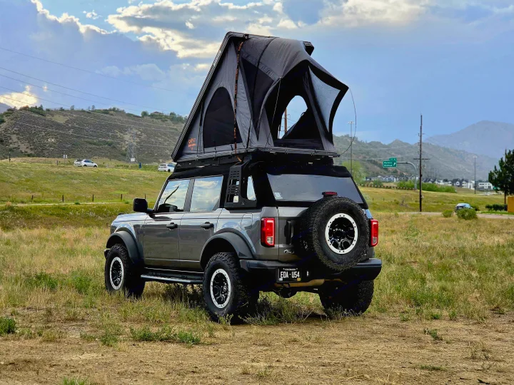Gray Ford Bronco with an open rooftop tent in a grassy field. An ideal RV rental for off-road camping and outdoor adventure.. Ford bronco 2021
