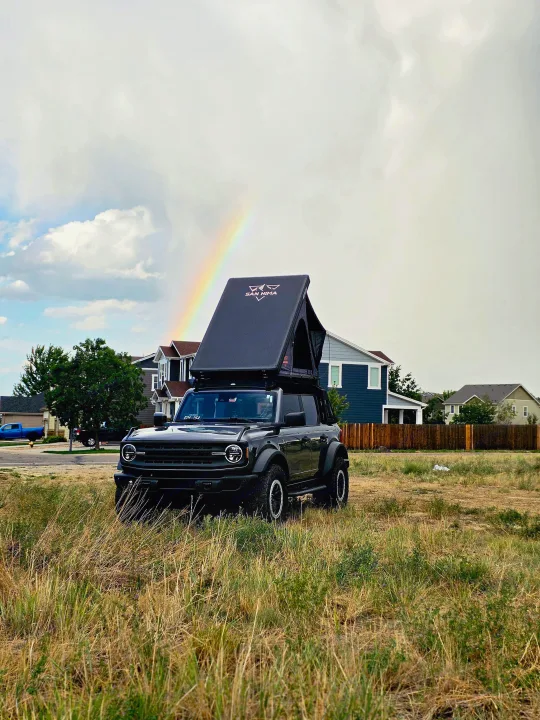 Black Ford Bronco with San Hima roof-top tent, great for RV rental adventures, parked in a field under a rainbow.. Ford bronco 2021