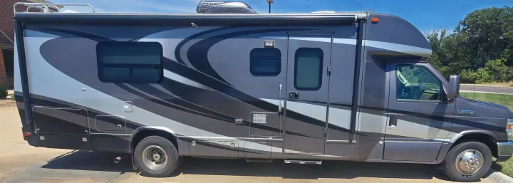 Dark gray Class C rv rental with swirly graphics, awning, and roof rack parked on pavement under a blue sky.. Phoenix Cruiser Phoenix Cruiser Motorhome 2013