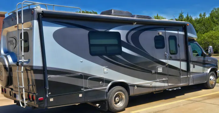 A gray Phoenix Cruiser RV rental with distinctive graphics, side storage, windows, and a rear ladder, parked outdoors.. Phoenix Cruiser Phoenix Cruiser Motorhome 2013