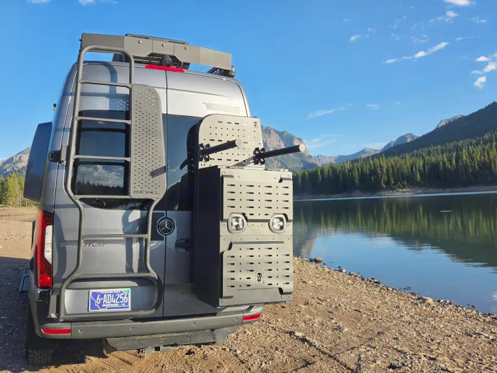 Winnebago Revel Sprinter RV rental by a serene mountain lake, featuring a ladder and gear storage for outdoor adventures.. Winnebago Revel 2025