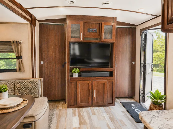 Explore a modern rv rental interior featuring a cozy dinette, entertainment center with TV, and inviting open entry door.. Forest River Surveyor 2018