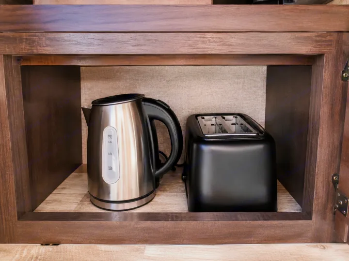 Essential kitchen appliances in this RV rental: an electric kettle and a toaster, neatly stored in a wooden cabinet.. Forest River Surveyor 2018