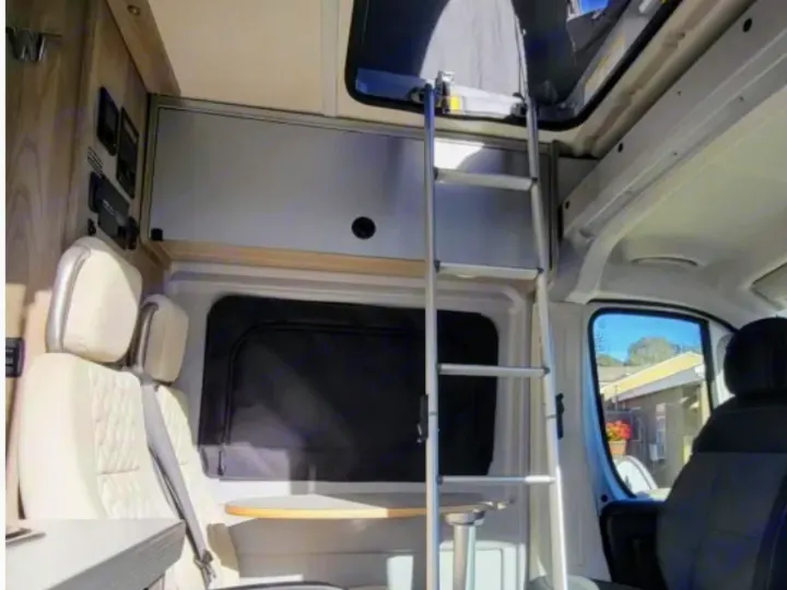 Inside this RV rental: a ladder to an upper bunk, comfy seating with a table, and overhead storage.. Winnebago Solis 2021