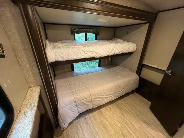 Spacious RV rental bunk beds with clean white comforters and windows revealing nature. A cozy camper interior for family sleeping.. Cruiser RV Shadow Cruiser 2018