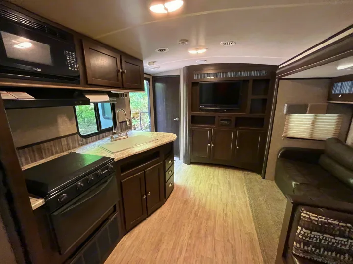 This RV rental offers a compact kitchen with a microwave, stove, and sink, flowing into a living area with a TV and sofa.. Cruiser RV Shadow Cruiser 2018