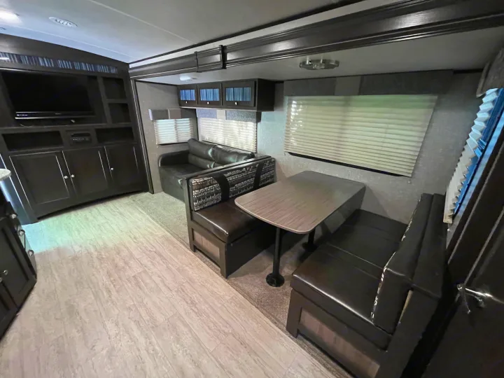Cozy RV rental living area with dark wood entertainment center, TV, sofa, and a dinette booth for comfortable travel.. Cruiser RV Shadow Cruiser 2018