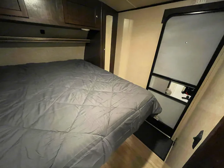 Cozy rv rental bedroom featuring a grey bed, overhead storage, and a partially open exterior door, ready for your adventure.. Cruiser RV Shadow Cruiser 2018
