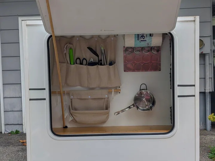 RV rental kitchen setup: Organized camper compartment with utensil holder, magnetic spice rack, paper towels, and saucepan.. MiniTrail Custom 2018