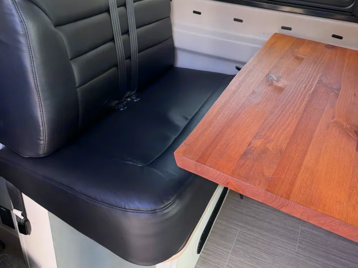 RV rental interior: black faux leather seating with seatbelts and a warm wooden table. A cozy dinette setup.. Dodge 3500shc 2021