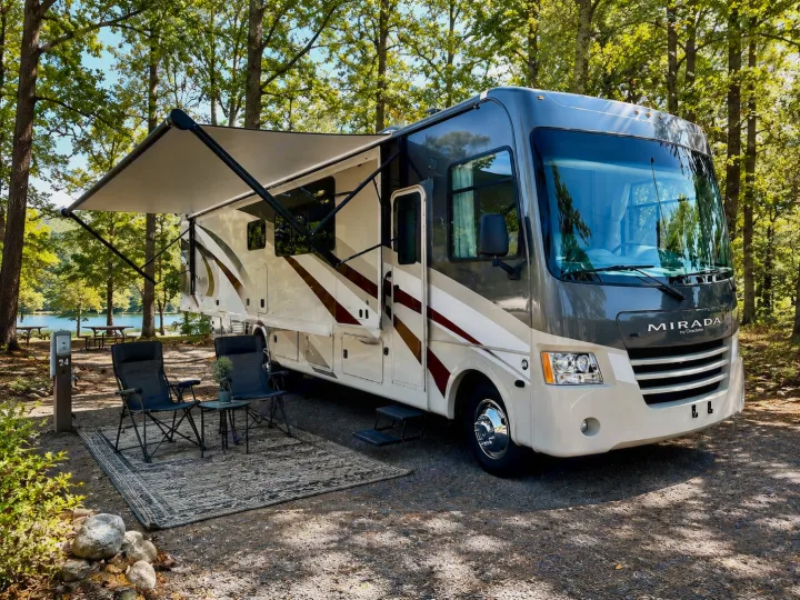 Beautiful rv rental at a serene lakeside campsite with an extended awning, outdoor chairs, and a table. Enjoy nature!. Coachmen Mirada 2019