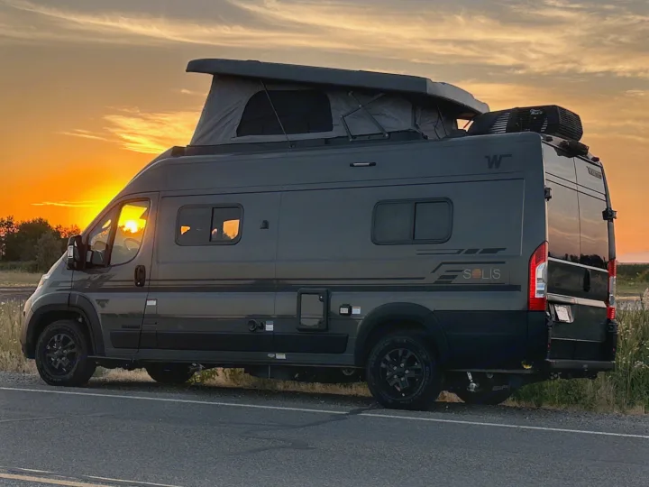 A gray Winnebago Solis rv rental camper van, with a pop-top roof, parked roadside under a glowing orange sunset.. Winnebago Solis 59PX 2027