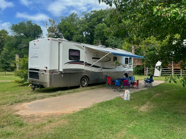 Enjoying a serene RV rental campsite with extended awning, outdoor seating, and lush trees. A doll relaxes on the grass.. Coachmen Cross Country 2003