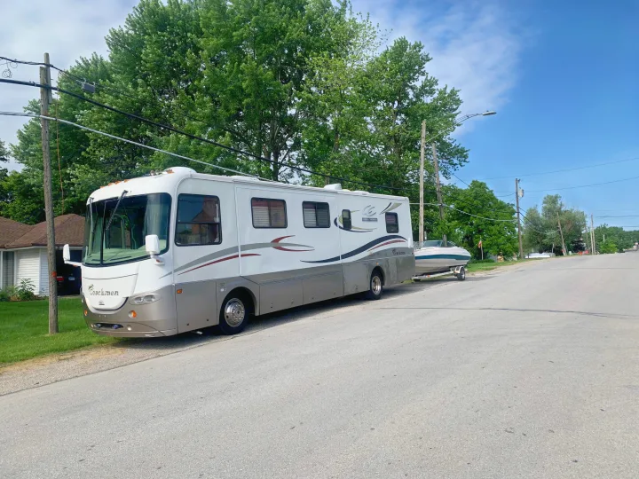 Coachmen RV with boat on trailer, parked on a street. Imagine your next adventure with an RV rental!. Coachmen Cross Country 2003