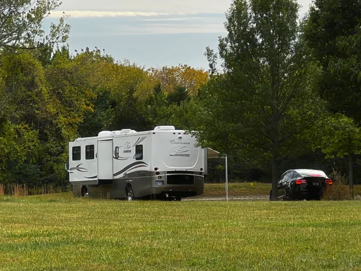 Coachmen RV rental, with slide-outs extended and awning deployed, parked in a lush, green campsite next to a black car.. Coachmen Cross Country 2003