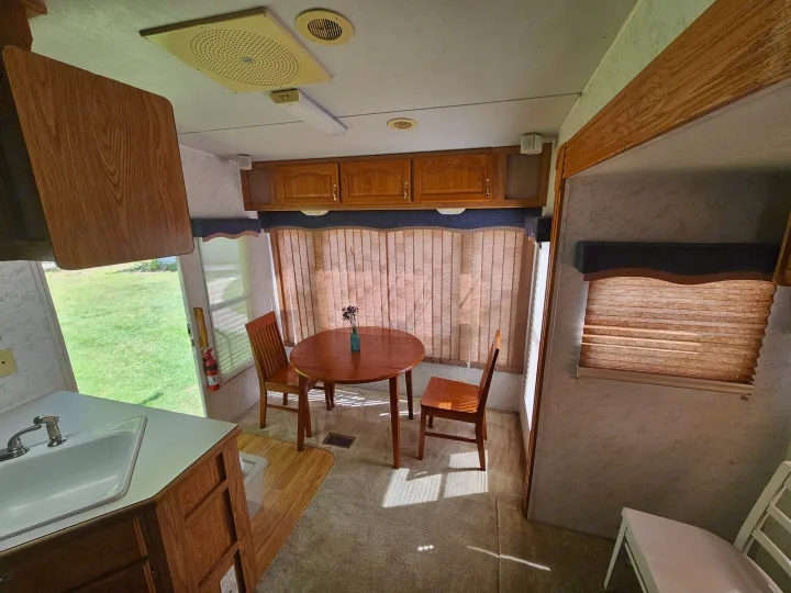 Cozy RV rental interior with dining table, chairs, kitchenette, and natural light. Perfect for travel trailer adventures.. Cedar Creek Cedar Creek Fifth Wheel 2002