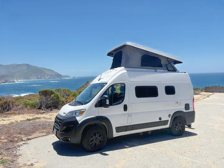 White Winnebago Solis Pocket rv rental with pop-top roof parked on a sunny cliffside overlooking the ocean and coast.. Winnebago Solis 2025