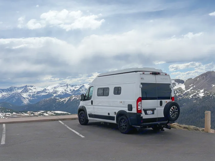 Experience mountain views with an rv rental. White camper van parked overlooking snow-capped peaks under clouds.. Winnebago Solis 2025