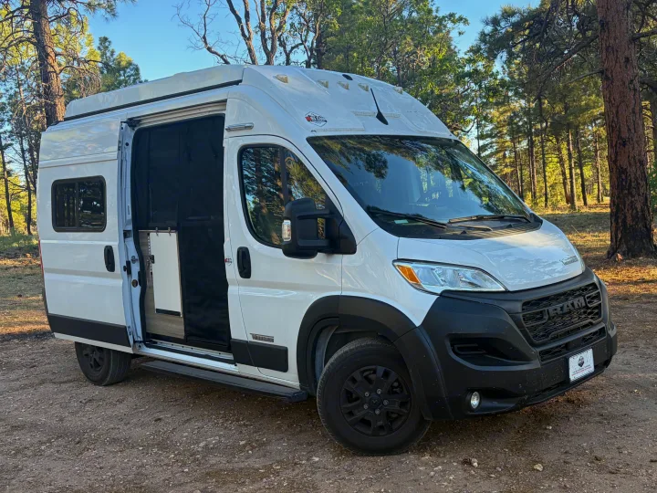 White RV rental camper van parked in a sunny forest, side door open to its interior, ready for adventures.. Winnebago Solis 2025