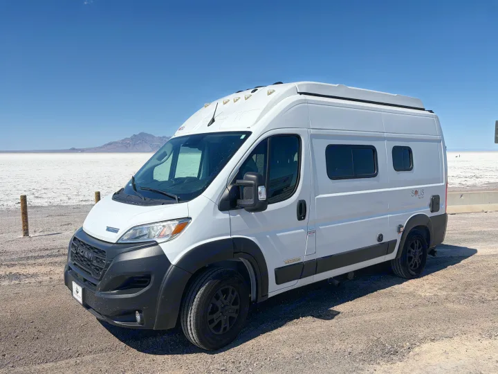 A white Winnebago Solis Pocket RV rental is parked on a vast, flat salt plain, with distant mountains under a clear blue sky.. Winnebago Solis 2025