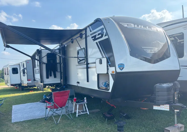 Camping with an RV rental! This Bullet travel trailer features an extended awning, outdoor seating, and a cozy rug on the grass.. Keystone RV Bullet Premium 2025