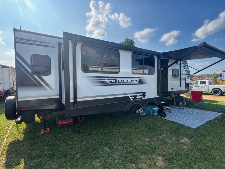 This RV rental, a Bullet travel trailer, is set up for camping with an extended slide-out and awning on a sunny day.. Keystone RV Bullet Premium 2025