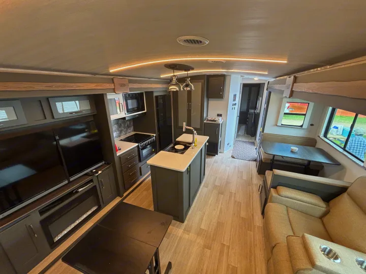 Explore this modern RV rental interior: full kitchen with island, living area with TV and fireplace, and dining booth.. Keystone RV Bullet Premium 2025