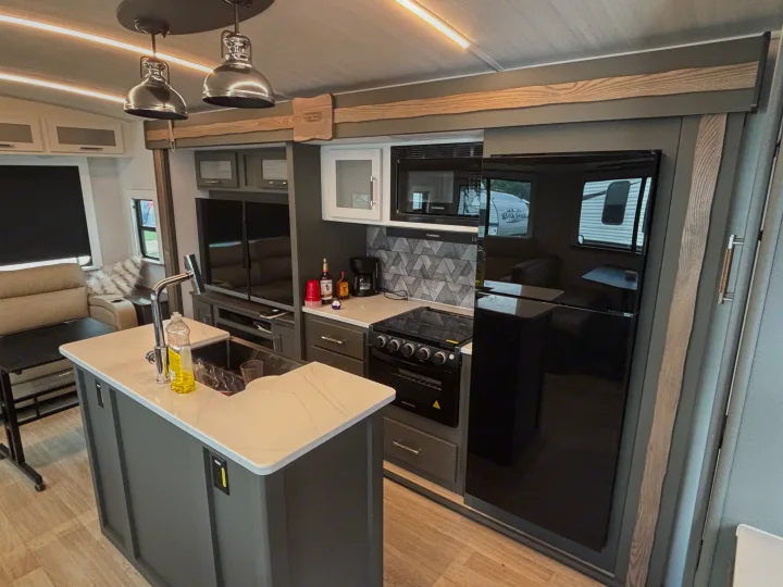 Step inside this modern rv rental, showcasing a sleek kitchen with an island, stove, and black refrigerator, ideal for travel.. Keystone RV Bullet Premium 2025