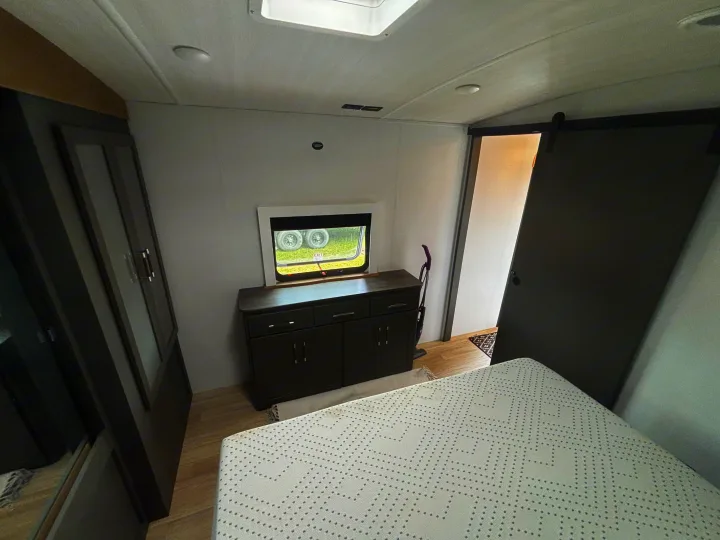 Experience comfort in this RV rental bedroom: large bed, dresser, storage, and stylish barn door. Ready for your travels!. Keystone RV Bullet Premium 2025