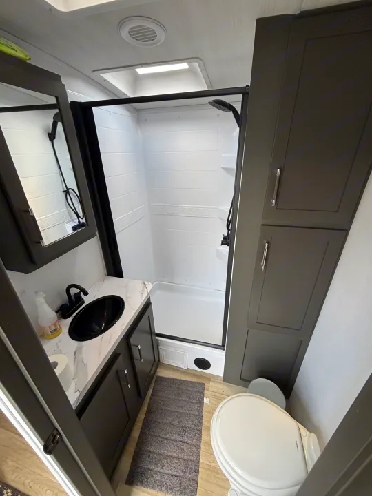 Clean, modern RV rental bathroom with a black-framed shower, vanity with sink, toilet, and ample storage cabinets.. Keystone RV Bullet Premium 2025
