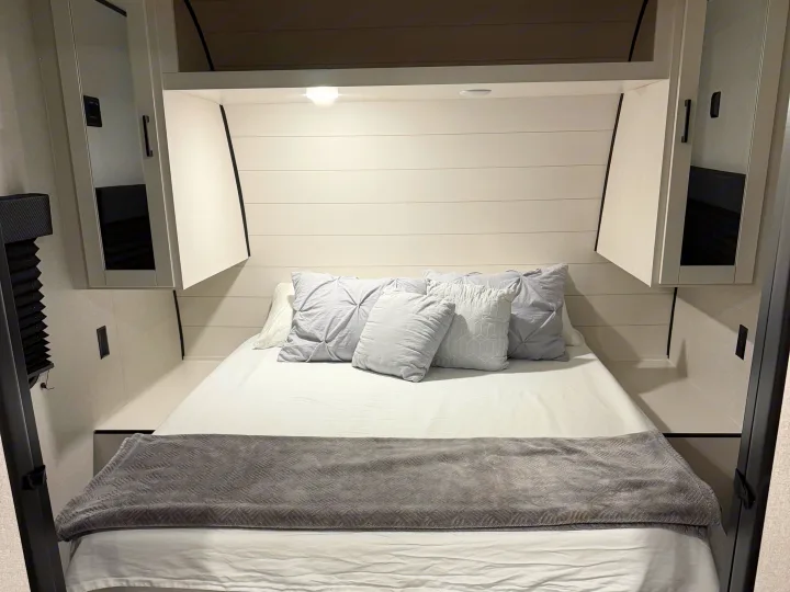 RV rental bedroom with a neatly made bed, white sheets, gray pillows, overhead cabinets, and wood-look flooring. Modern travel trailer interior.. Jayco Jay-flight 2026
