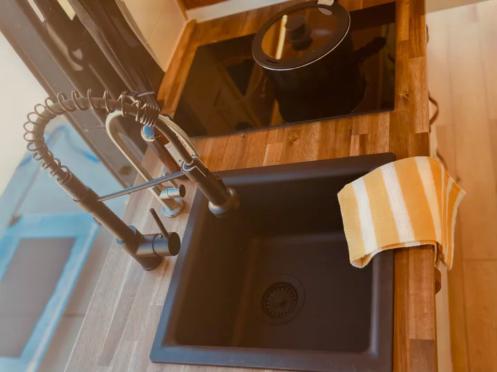 Inside an RV rental: a modern kitchenette featuring a black sink, coiled pull-down faucet, induction cooktop, and wood counters.. Mercedes Sprinter 2500 2019