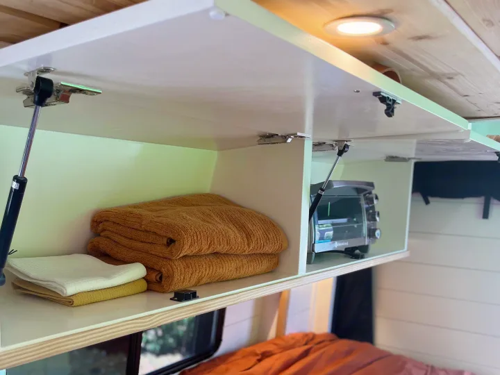 Inside an RV rental: Smart overhead storage with fresh towels & a convenient toaster oven. Essential comforts for your travels.. Mercedes Sprinter 2500 2019
