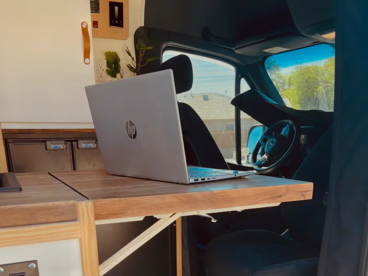 RV rental mobile office: An HP laptop sits on a fold-out wooden table inside a camper van, showcasing the remote work setup.. Mercedes Sprinter 2500 2019