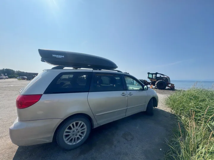 Minivan with roof box by the sea, ready for adventure. Heavy machinery on beach, offering a journey like a compact rv rental.. Toyota Sienna 2009