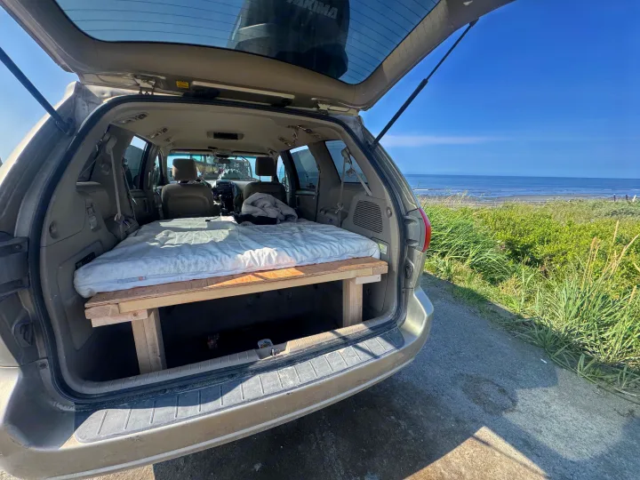 Minivan with a DIY bed platform for an RV rental adventure, offering a cozy sleep space and scenic ocean view.. Toyota Sienna 2009