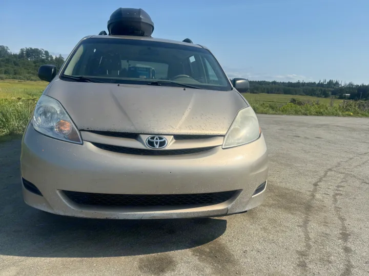 Gold Toyota Sienna minivan with roof cargo box, perfect for an rv rental road trip adventure, parked outdoors on a sunny day.. Toyota Sienna 2009