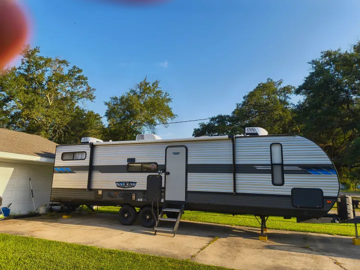 Large Salem travel trailer (RV rental) parked on a paved driveway next to a house, with trees and blue sky.. Forest River Salem 2021